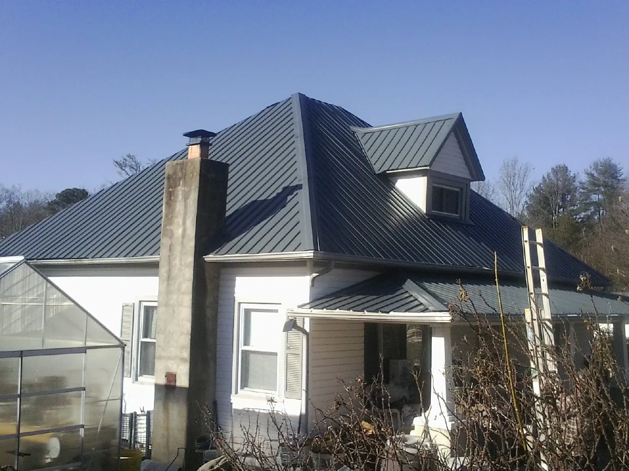 Dark blue standing seam metal roof on a white farmhouse with dormer — Slate & Tile Roof Repair by Roofing Brothers in Milltown