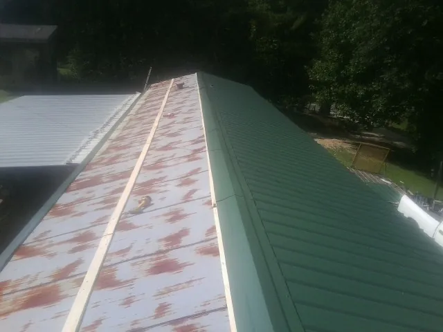 Old rusted panels beside newly installed green metal roofing — Wind Damage Roof Repair by Roofing Brothers in Milltown