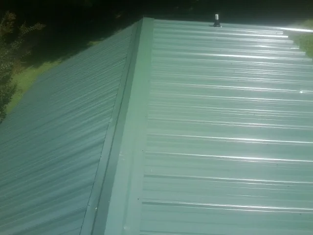 New green metal panels meeting at the ridge of a roof — Flat Roof Repair work by our crew in Milltown