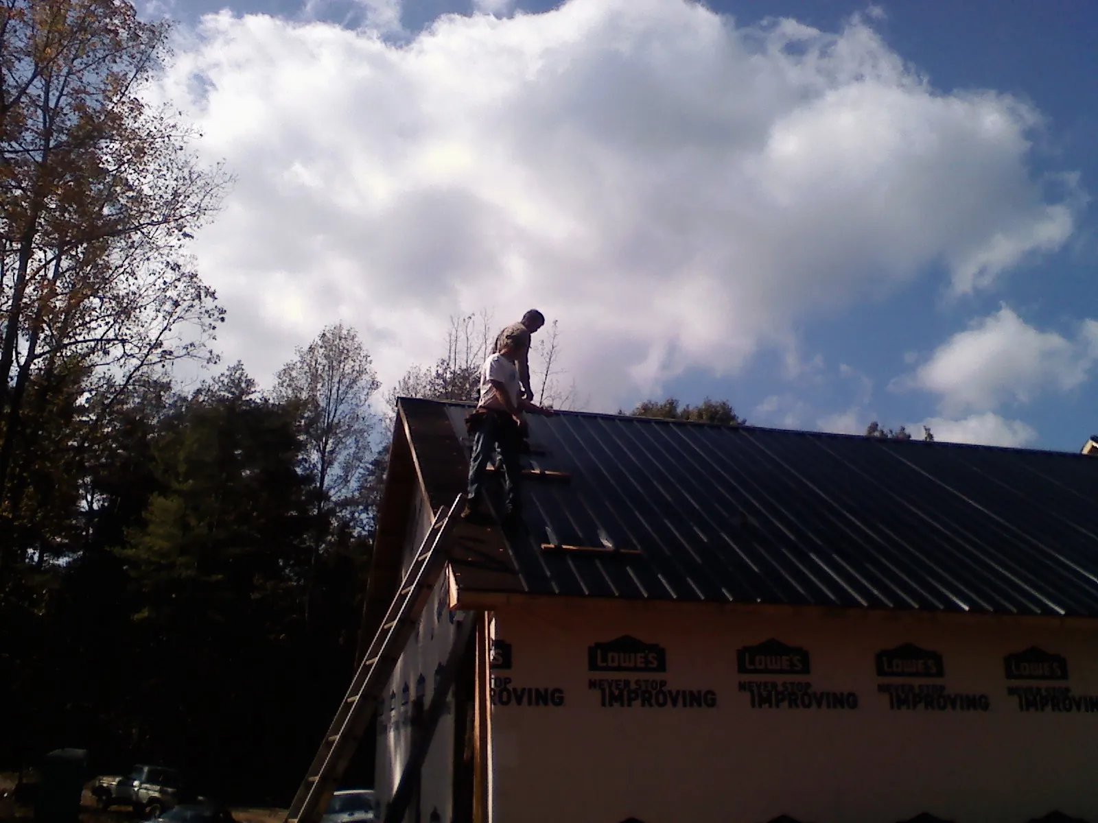 Roofer fastening dark metal panels high against a cloudy sky, from a Roof Inspection job in Milltown