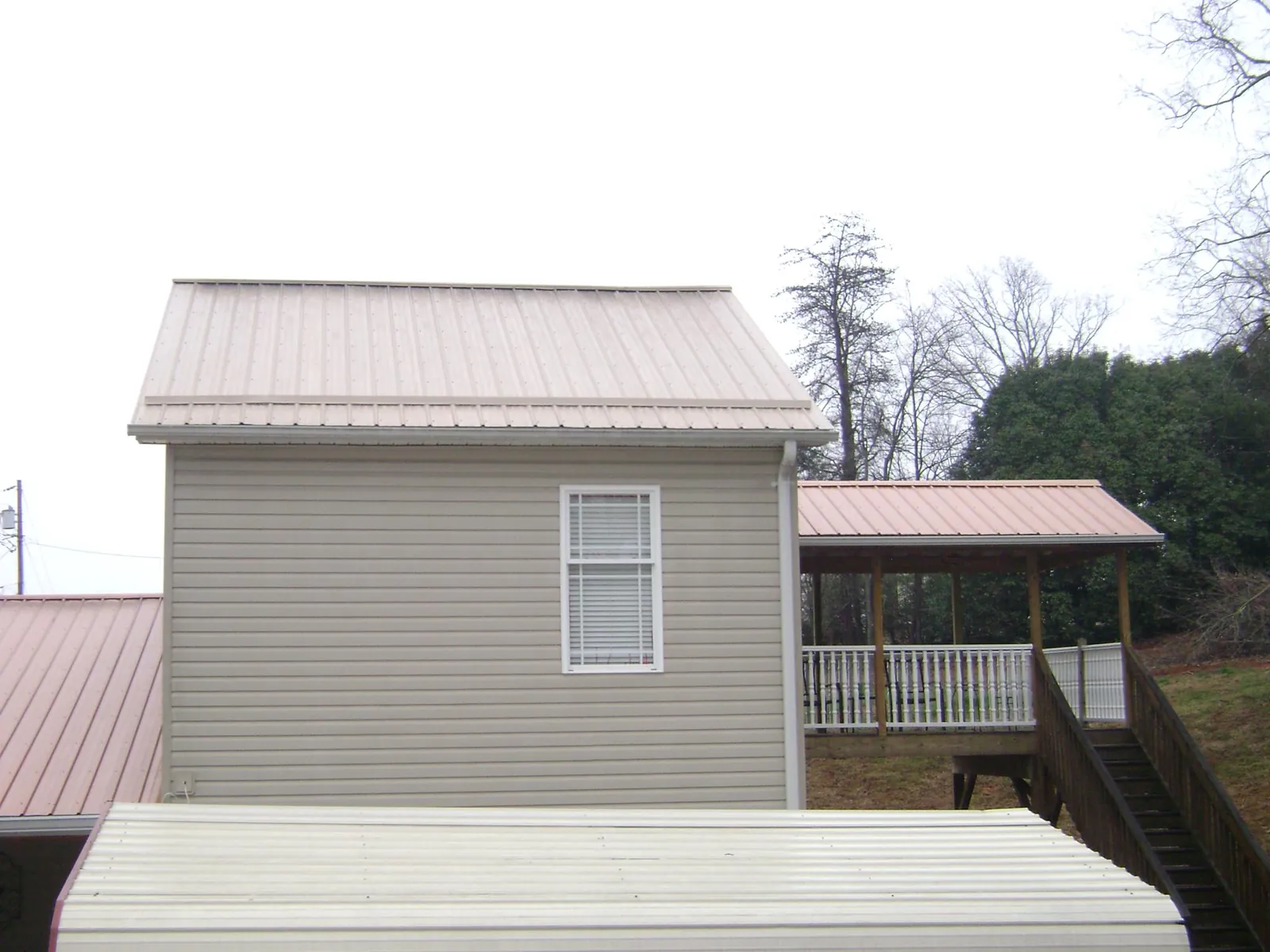 Tan metal roofs on a two story addition and attached porch, from a Roof Replacement job in Milltown